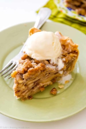 slice of apple crumble pie with a scoop of vanilla ice cream on a light green plate with a fork