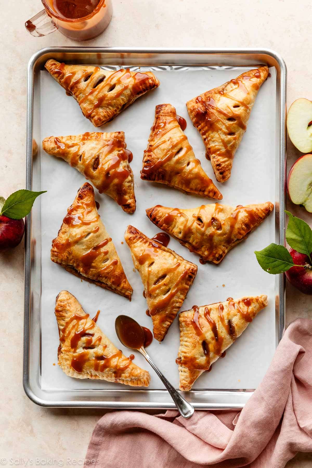 apple turnovers on lined baking sheet with caramel sauce on top.