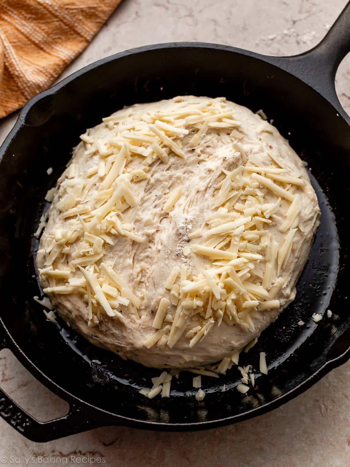 shredded cheese on top of round dough in cast iron skillet.