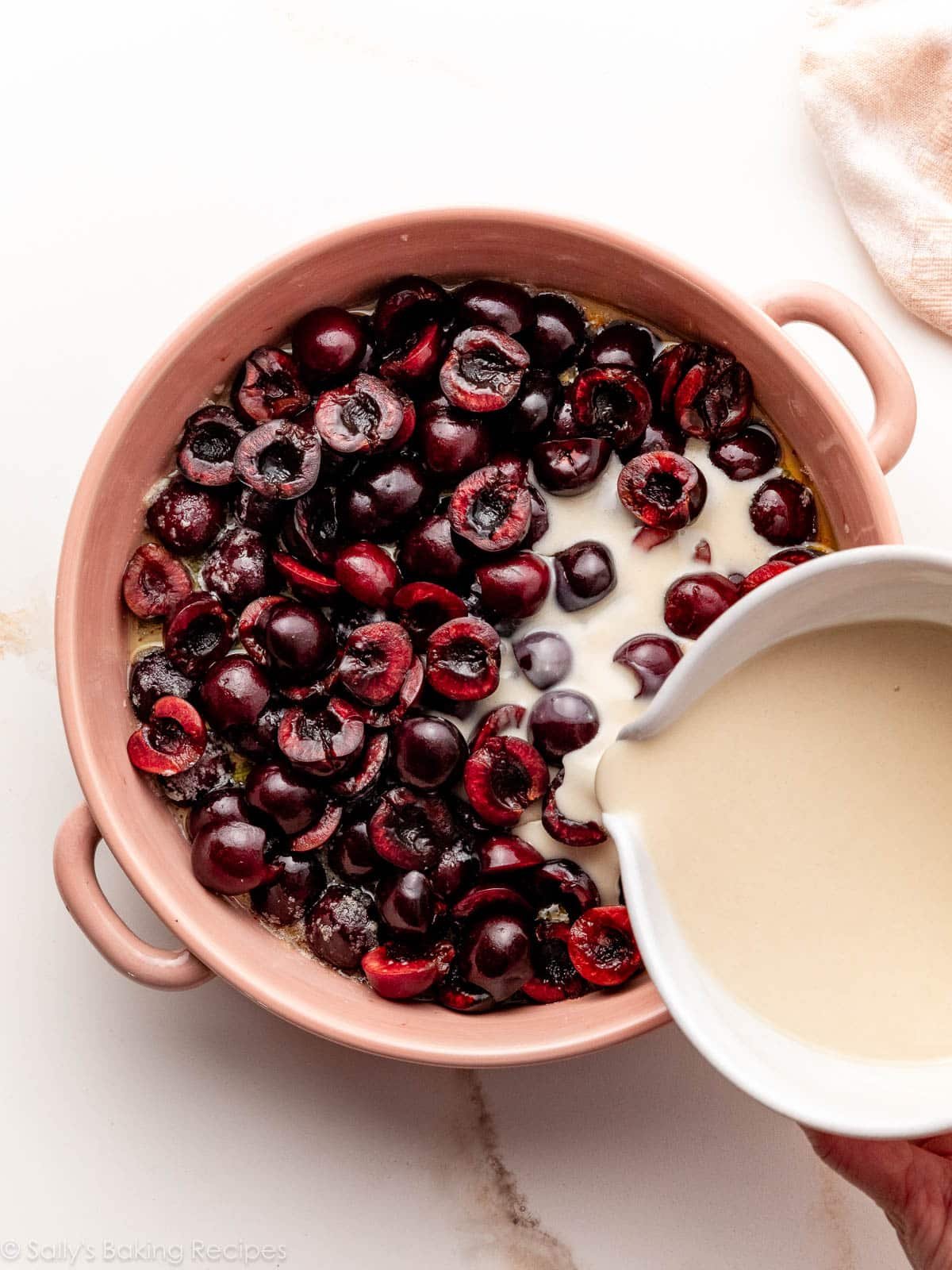 pouring batter over fruit in pink baking dish.