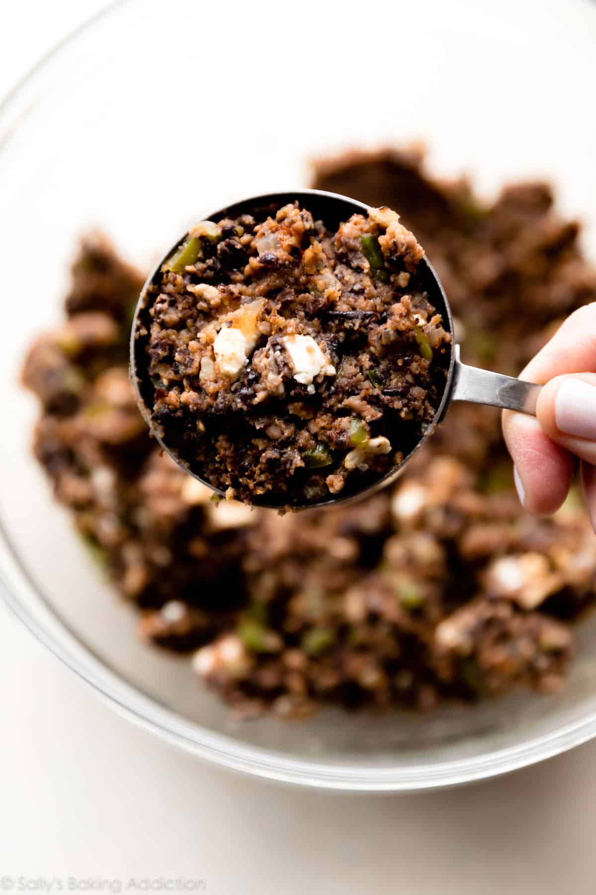 hand holding a measuring cup filled with black bean burger mixture