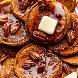 close-up of pumpkin pancakes with slices of butter and maple pecan syrup on top.