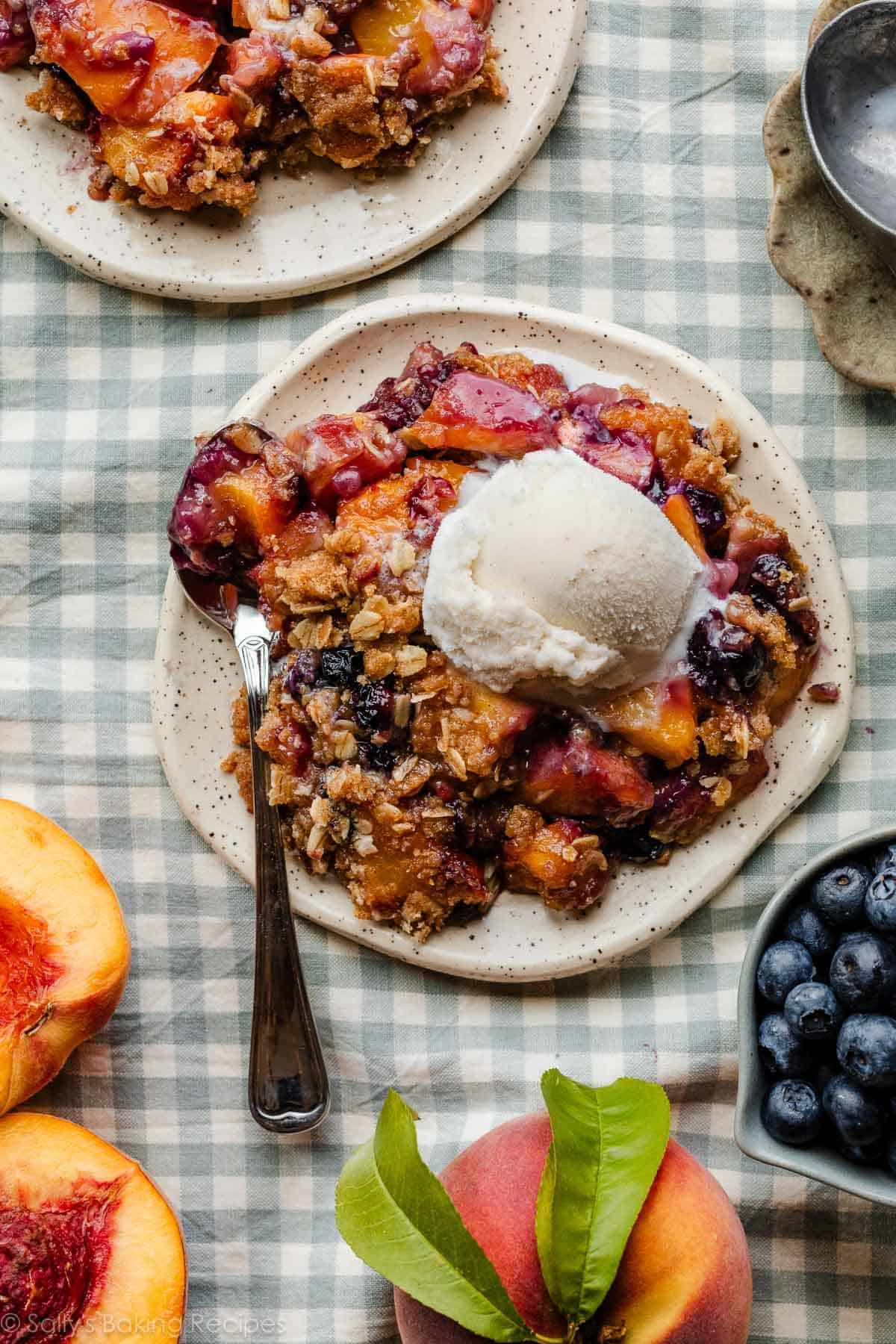 blueberry peach crisp with brown butter oat topping and vanilla ice cream on plates on blue gingham linen.