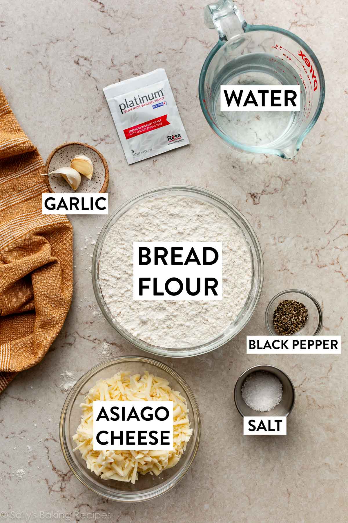 ingredients in bowls on marble surface including flour, water, yeast, garlic, and cheese.