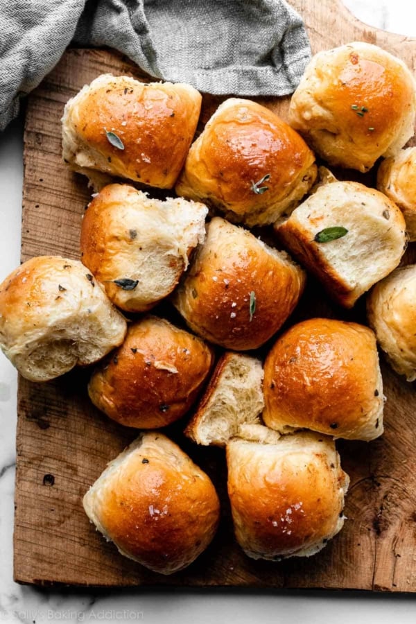 dinner rolls garnished with fresh chopped sage on wooden cutting board.