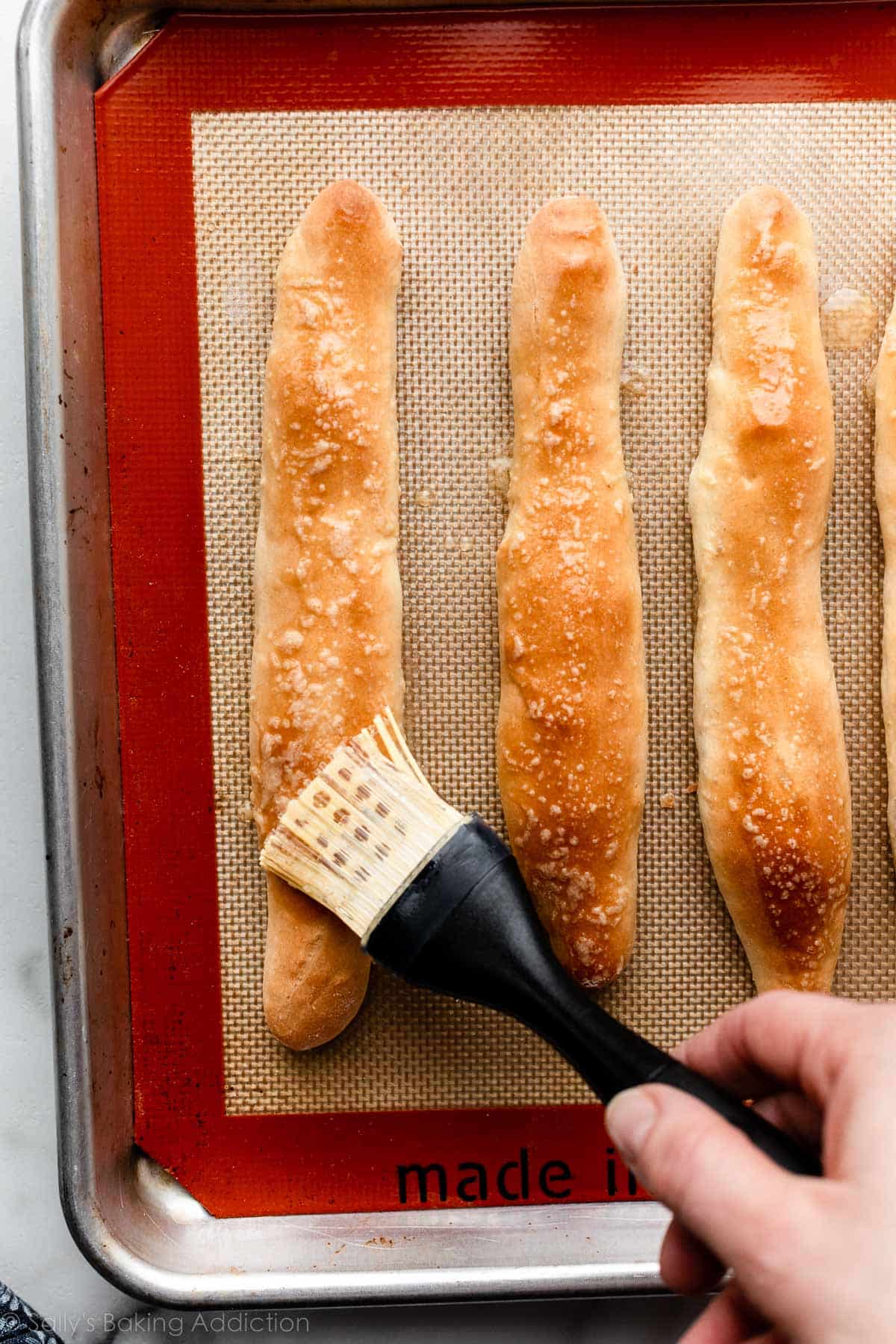 brushing butter on 3 homemade breadsticks.