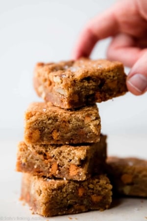 stack of 4 butterscotch blondies with a hand taking the top blondie