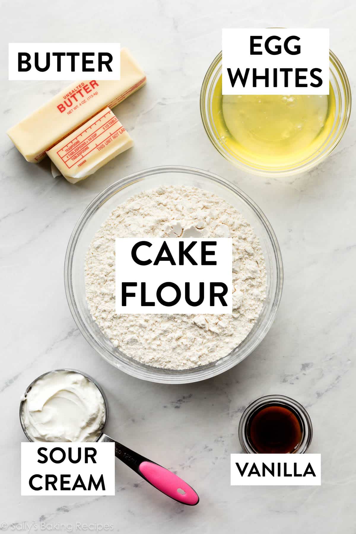 ingredients on marble counter including vanilla, sour cream, egg whites, cake flour, and butter.