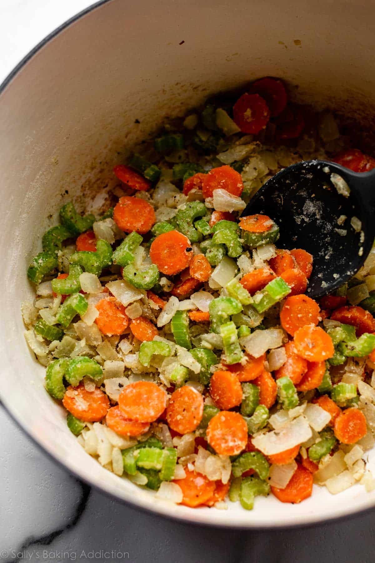 carrots, celery, and onions mixed with herbs in big pot.