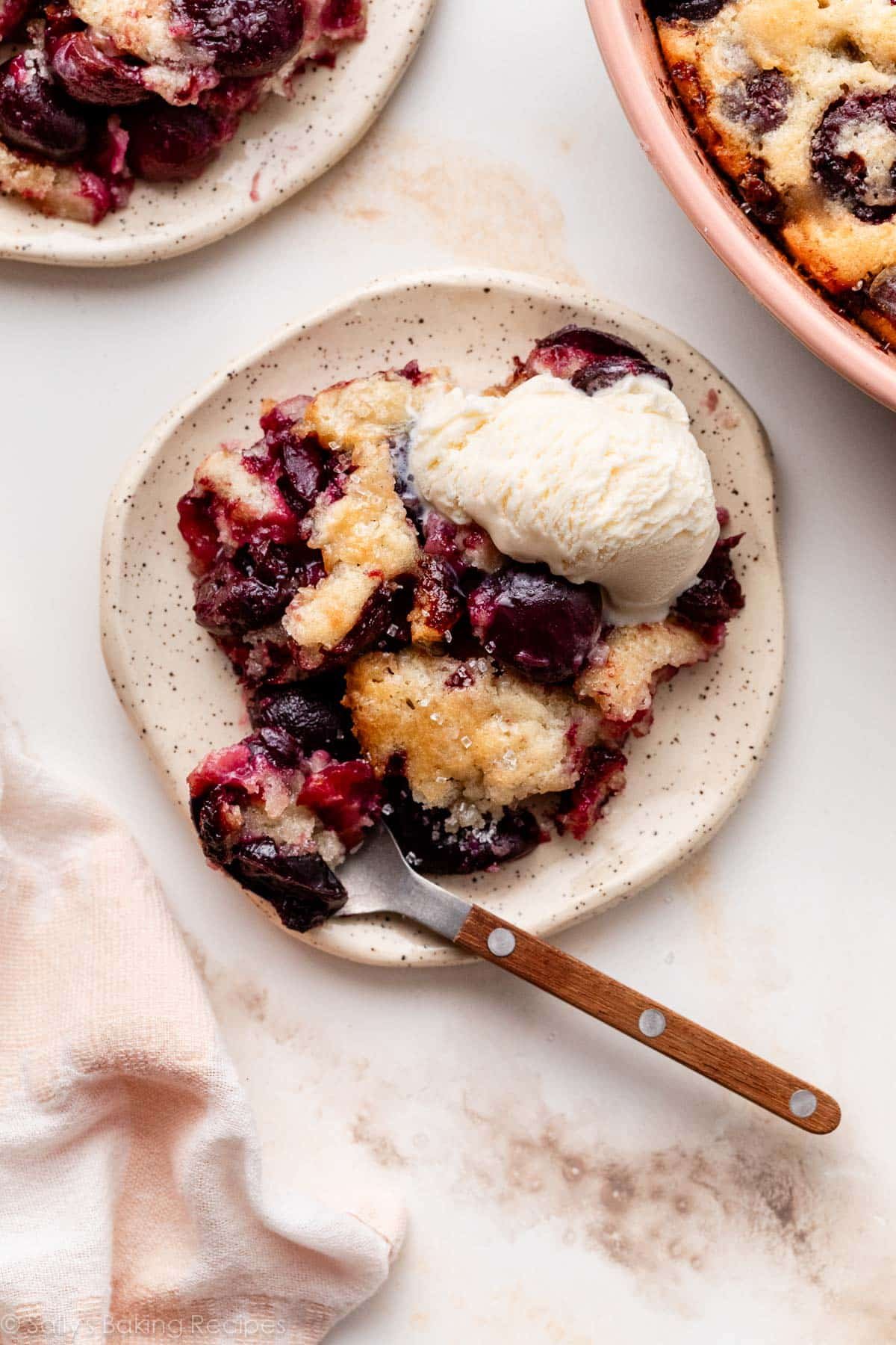 cherries cobbler on plate with spoon and vanilla ice cream.