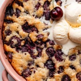 cherry cobbler in pink ceramic baking dish.