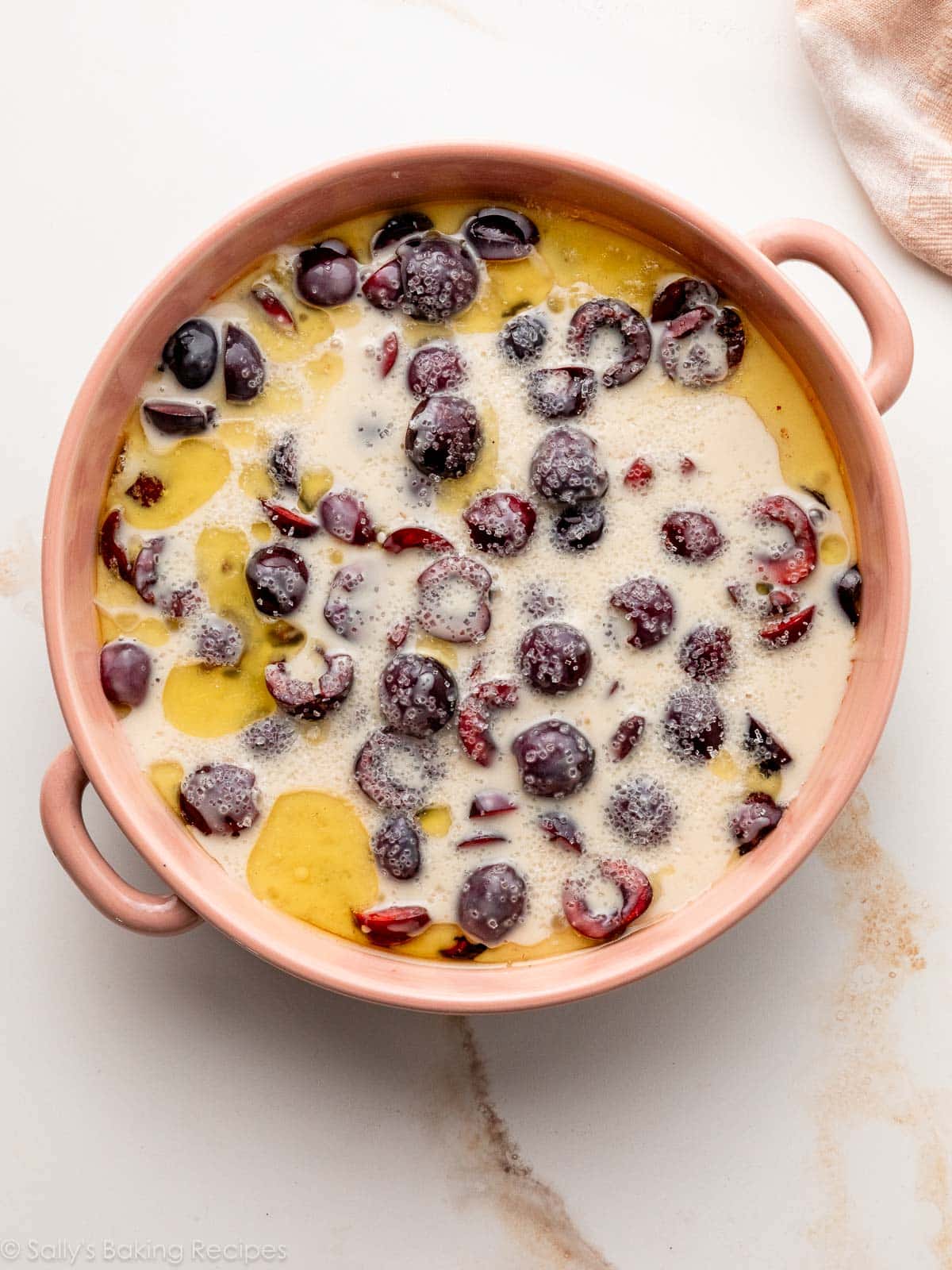 batter and melted butter with cherries in baking dish.