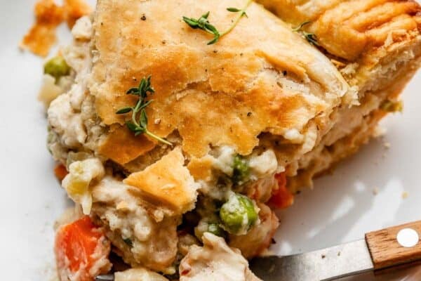 slice of double crust chicken pot pie with golden flaky pie crust on white plate with fork that has a wooden handle.