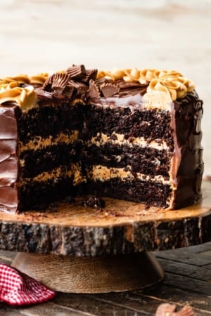 3 layer chocolate cake with peanut butter frosting and dark chocolate ganache on wood cake stand.