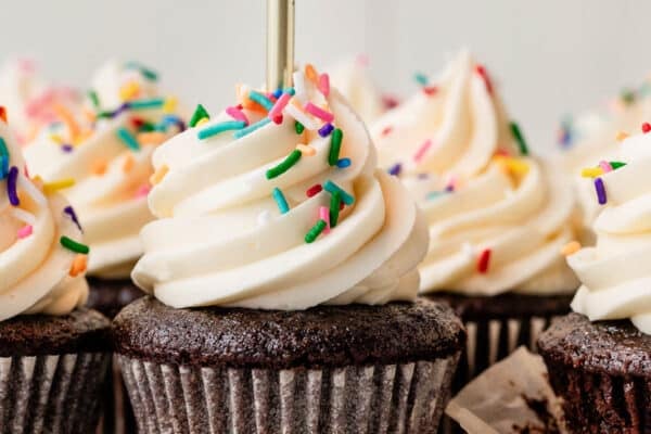 chocolate cupcakes with vanilla buttercream, rainbow sprinkles, and a gold birthday candle.