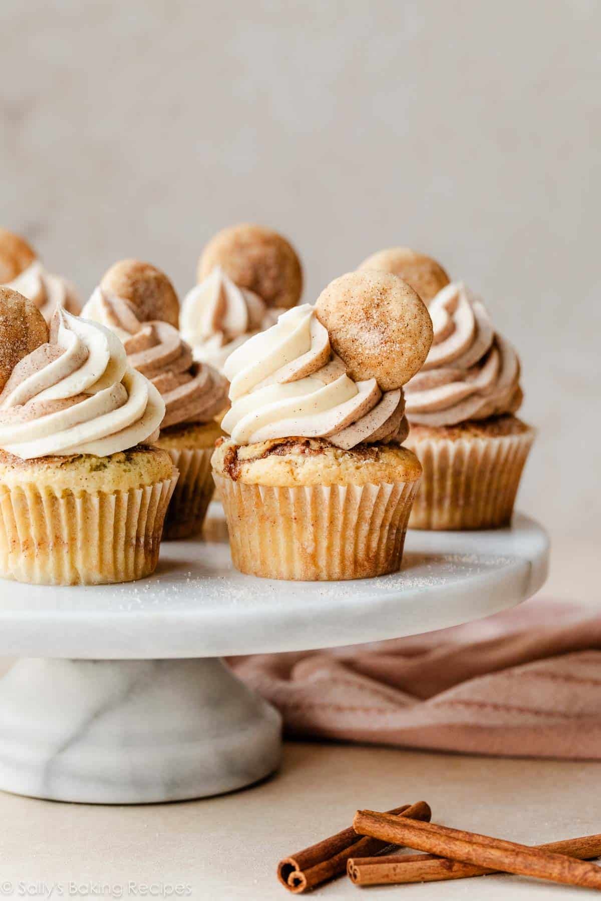 snickerdoodle cupcakes with mini snickerdoodle cookies as garnish on a marble cake stand.