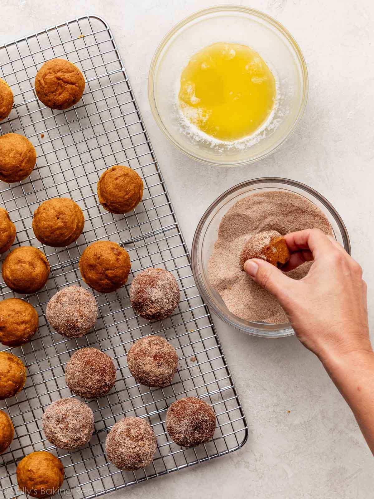 hand dipping mini muffin in cinnamon and sugar mixture.