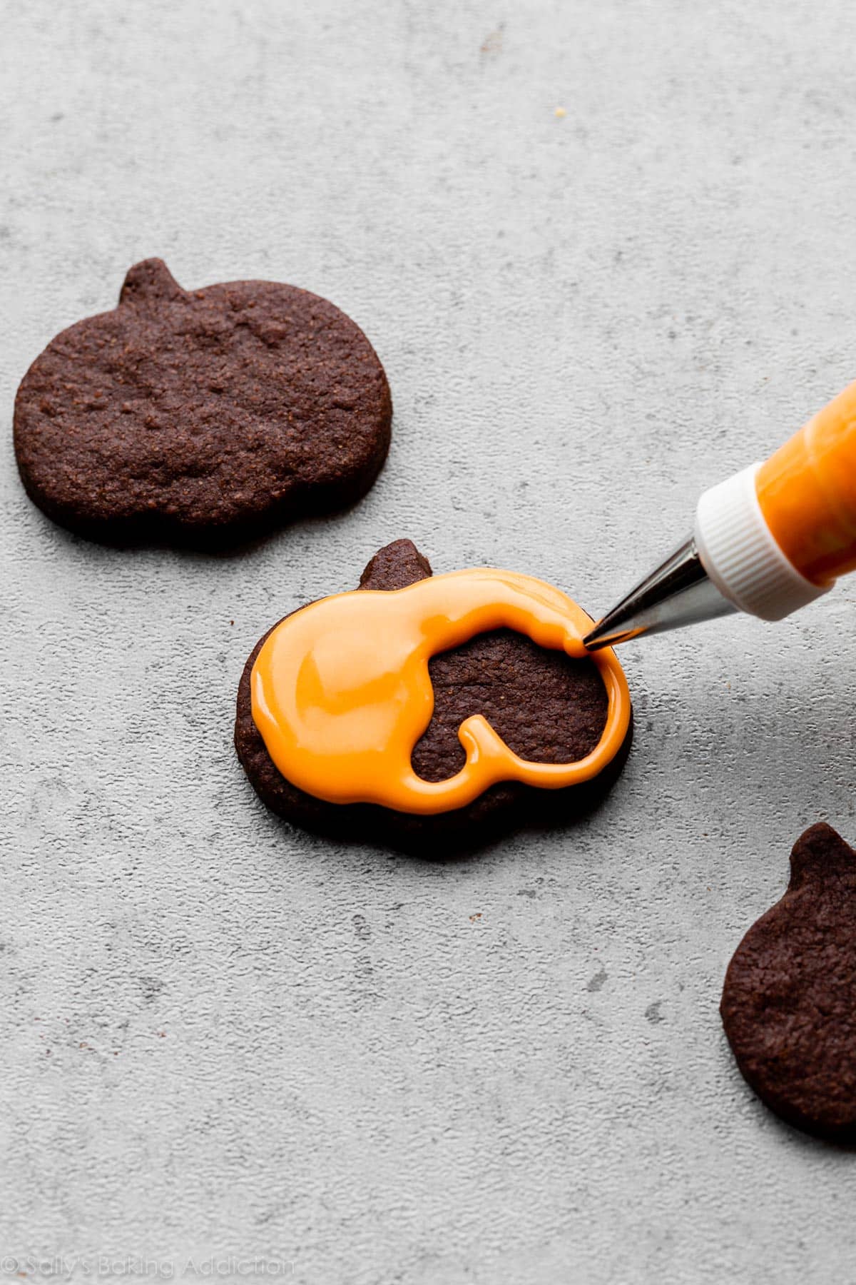 piping orange royal icing on a chocolate pumpkin shaped cookie