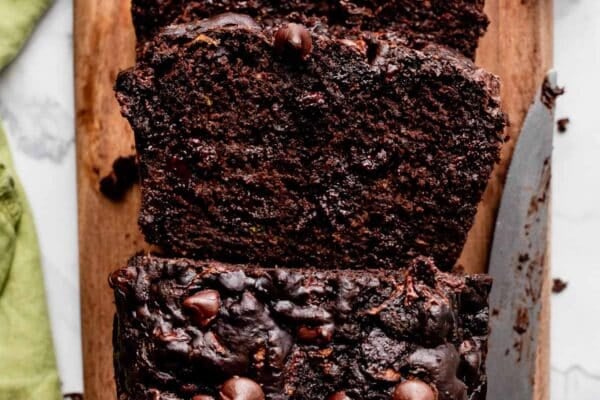 loaf of chocolate zucchini bread with chocolate chips cut with 2 slices on wooden cutting board.