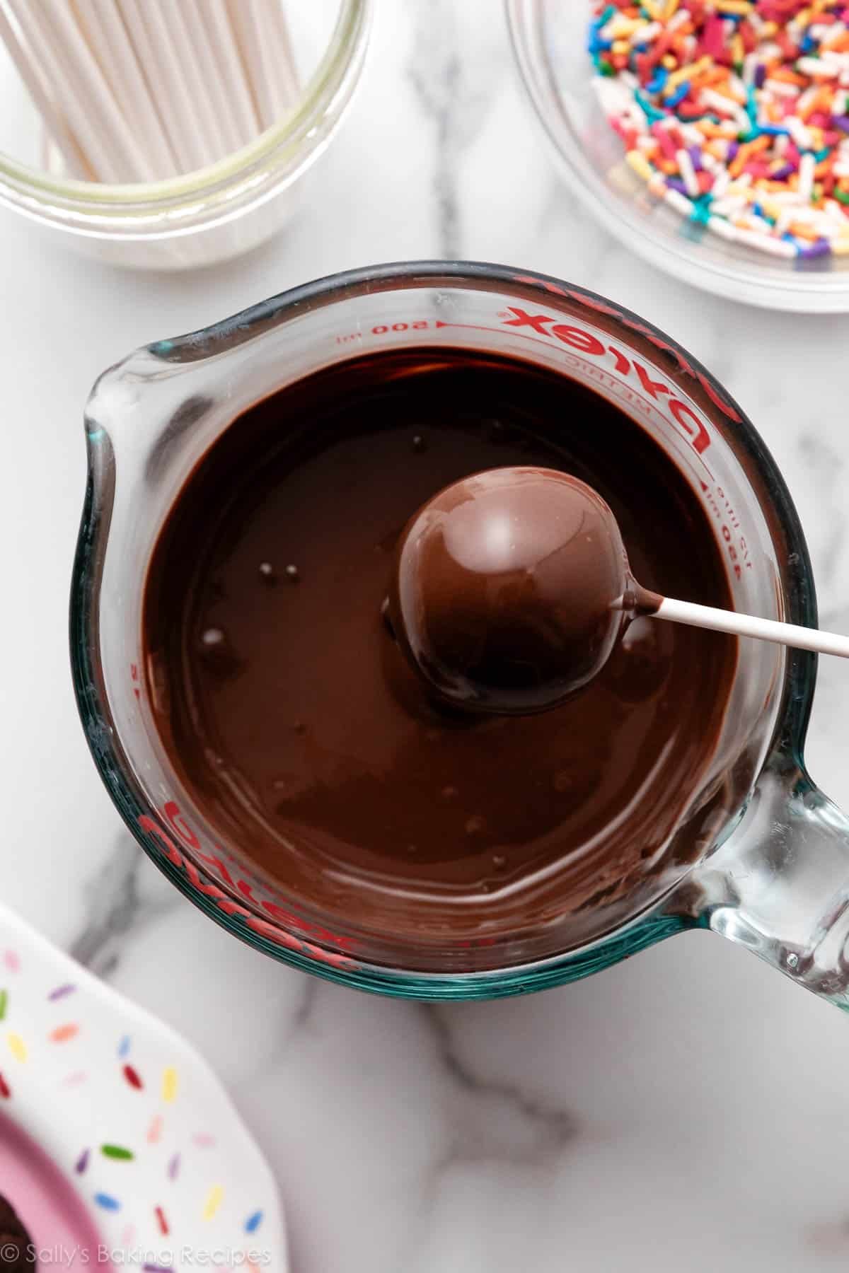 ball on lollipop stick being dipped in chocolate.