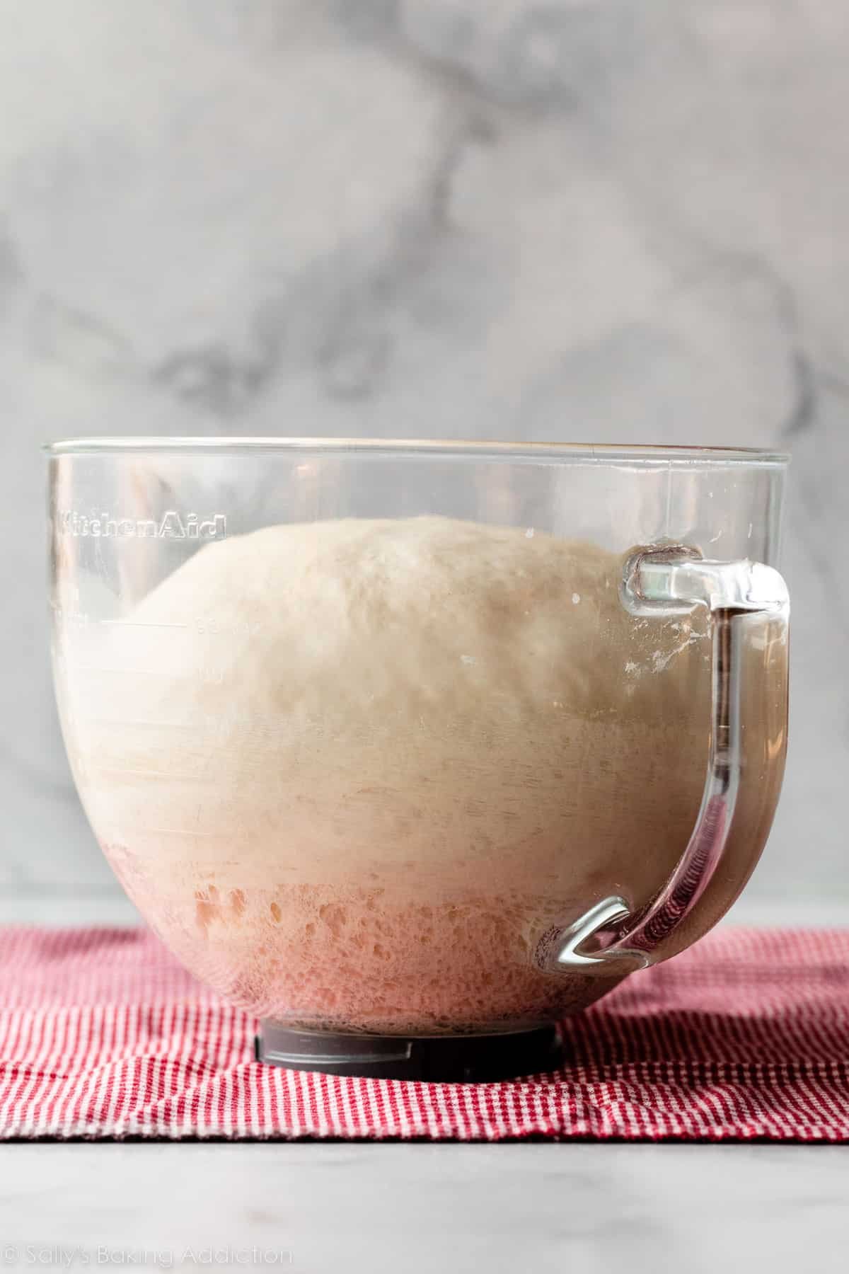 risen dough in glass bowl set on red checkered linen.