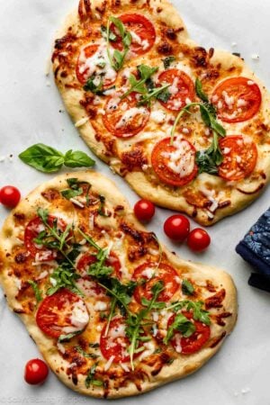 homemade flatbread pizza with mozzarella cheese, tomatoes, and arugula on top.