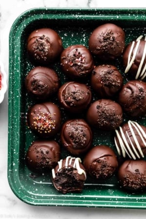 chocolate covered oreo balls truffles topped with crushed Oreo cookie crumbs and arranged on green baking sheet.