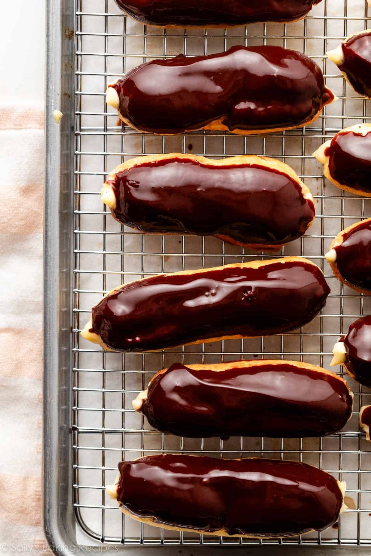 chocolate ganache-topped eclairs on cooling rack.