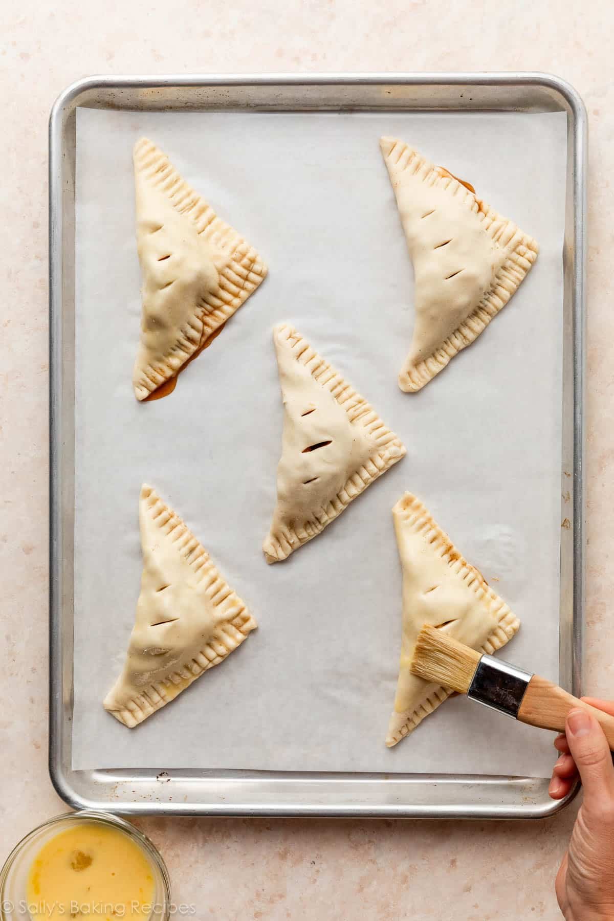 shaped apple turnovers on lined baking sheet.