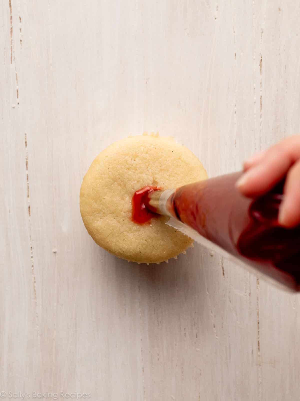 piping tip and bag filling cupcake with jelly.