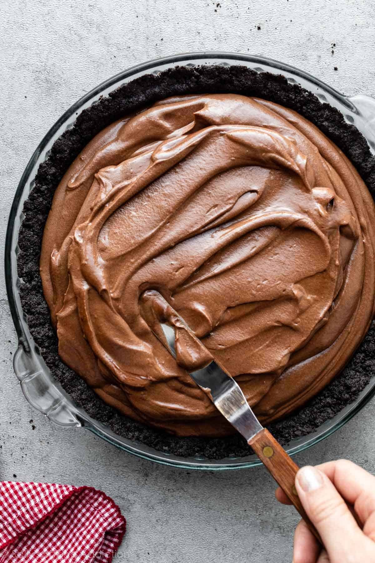 spreading chocolate mousse filling in oreo crumb crust in pie dish.