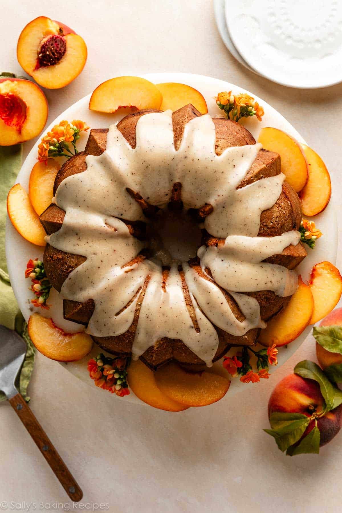 peach Bundt cake with brown butter icing on cake stand with fresh peach slices around it.