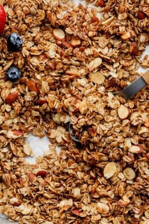 homemade vanilla almond granola spread on lined baking sheet with a couple fresh strawberries and blueberries.