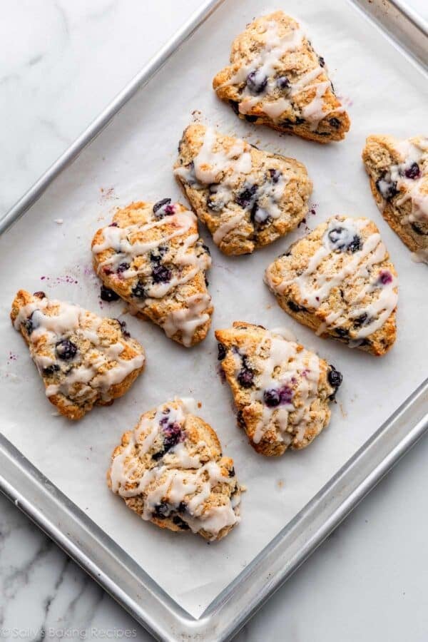 blueberry scones with icing on lined baking sheet.