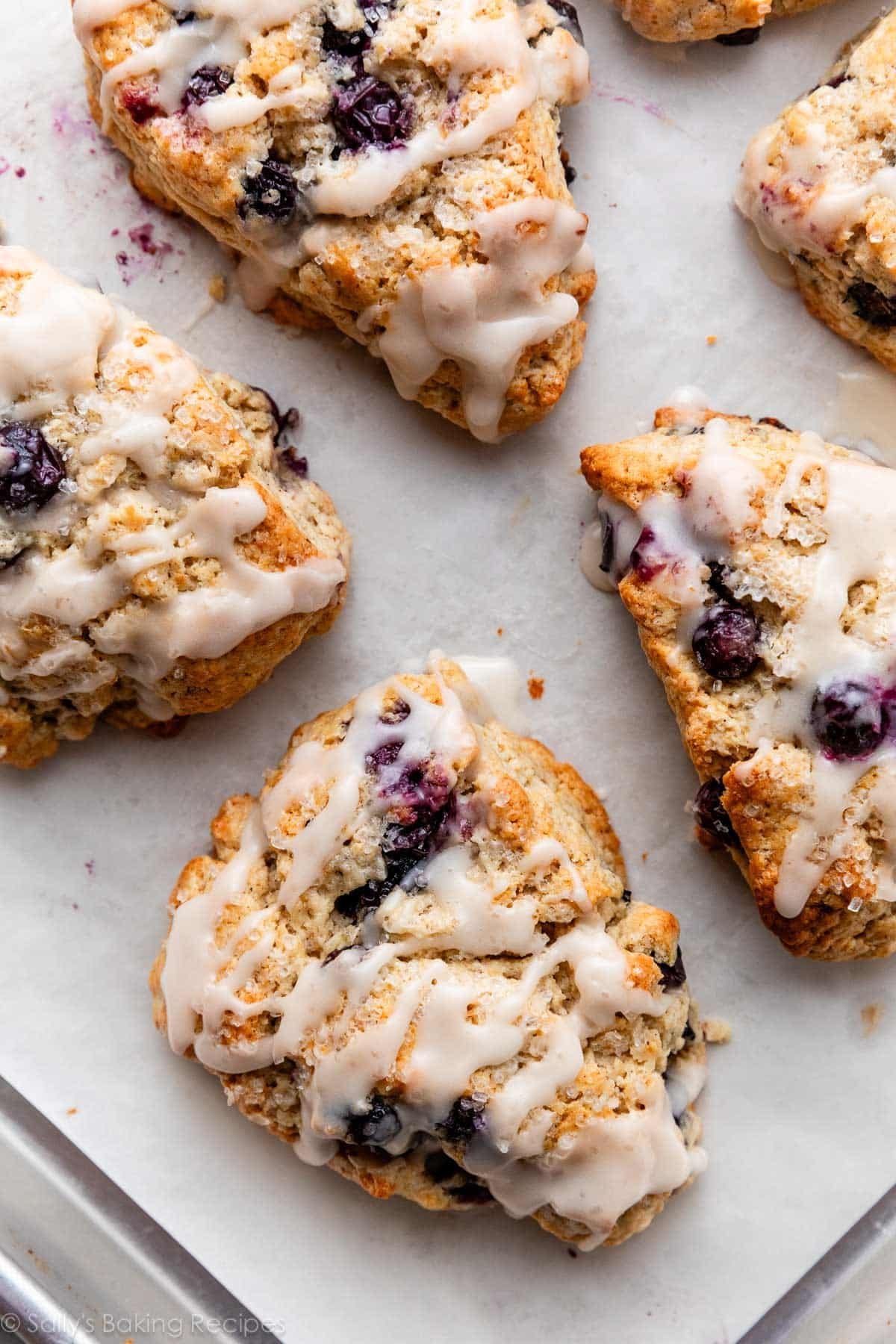 blueberry scones with icing on lined baking sheet.