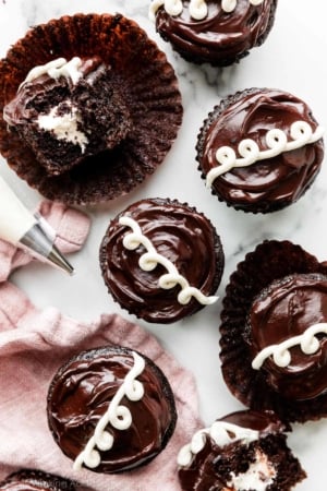 7 cream-filled chocolate cupcakes on marble counter with pink linen in left bottom corner.