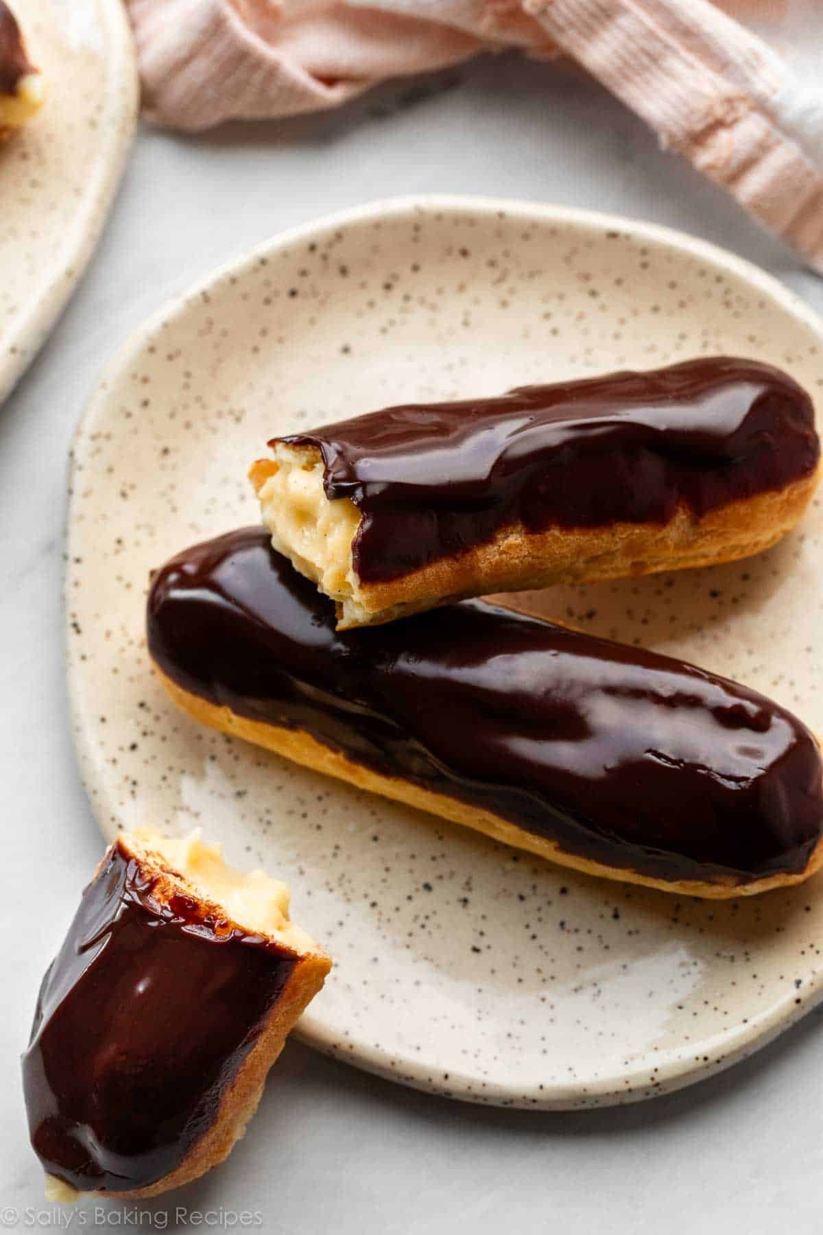 two eclairs on plate with one bitten into.