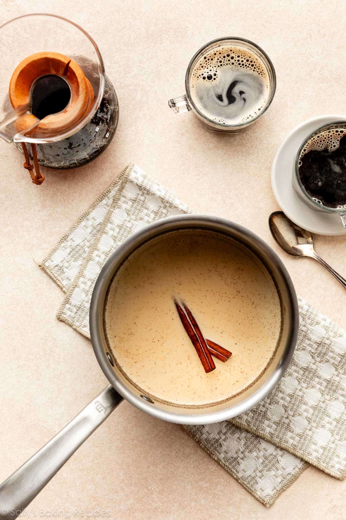 cream mixture in pot with cinnamon sticks on beige-patterned linen.