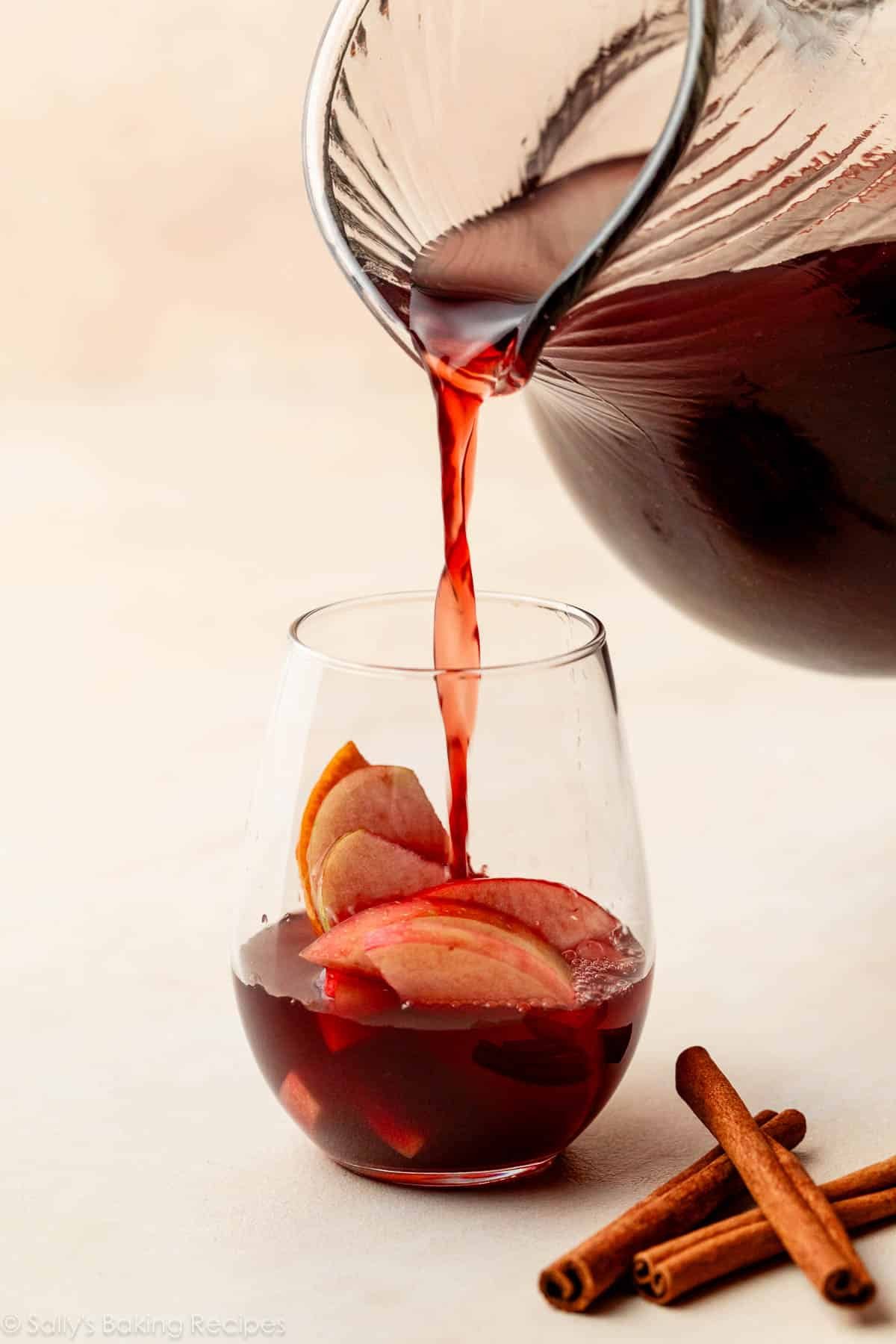 pouring red sangria over glass of sliced apples.