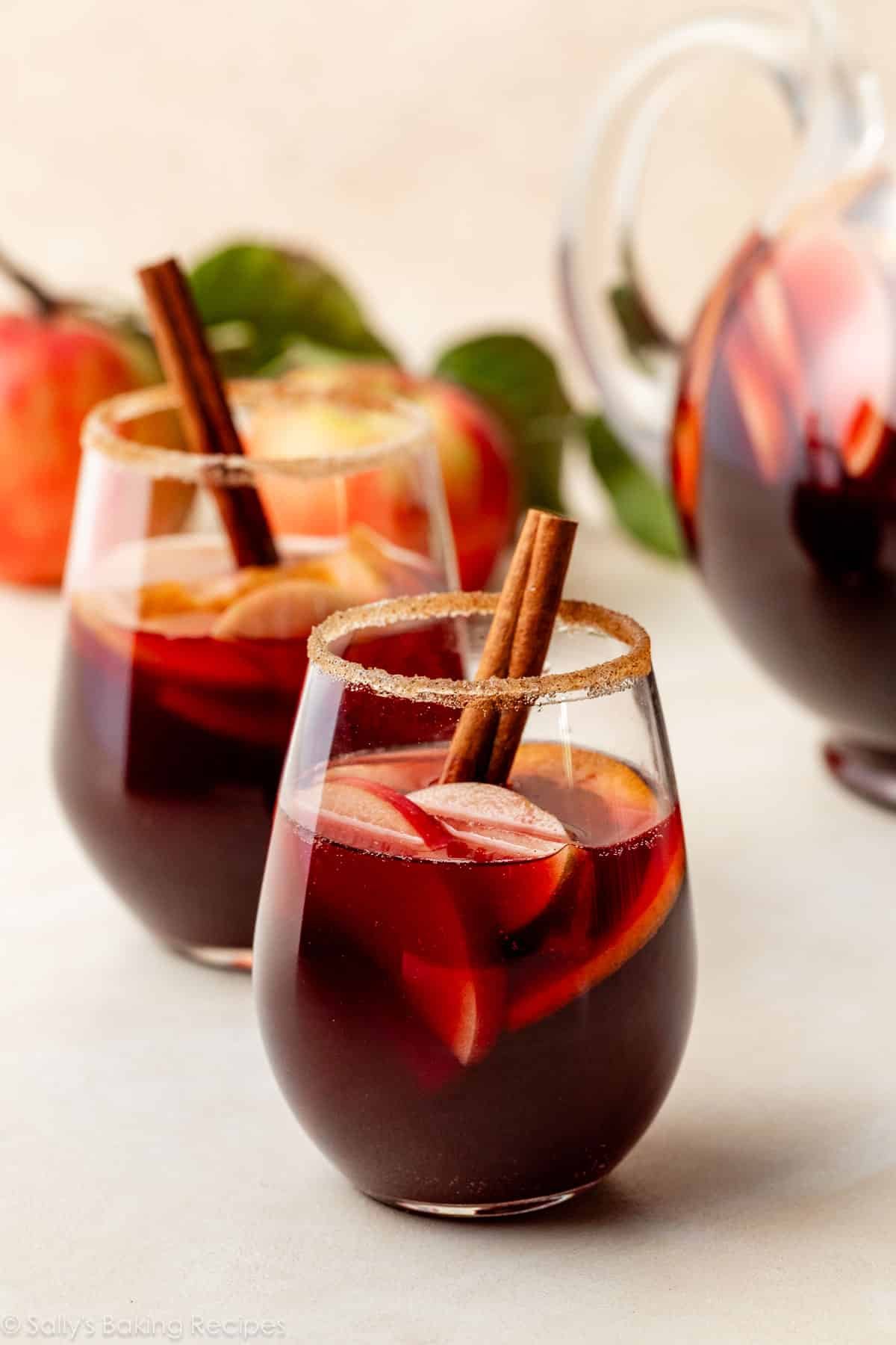 red apple sangria with cinnamon stick and cinnamon-sugar rim in stemless wine glass.