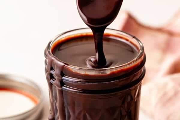 hot fudge sauce being drizzled from spoon into jar.