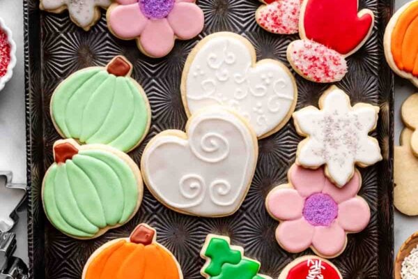 decorated sugar cookies on baking sheet including hearts, pumpkins, trees, mittens, and flowers.