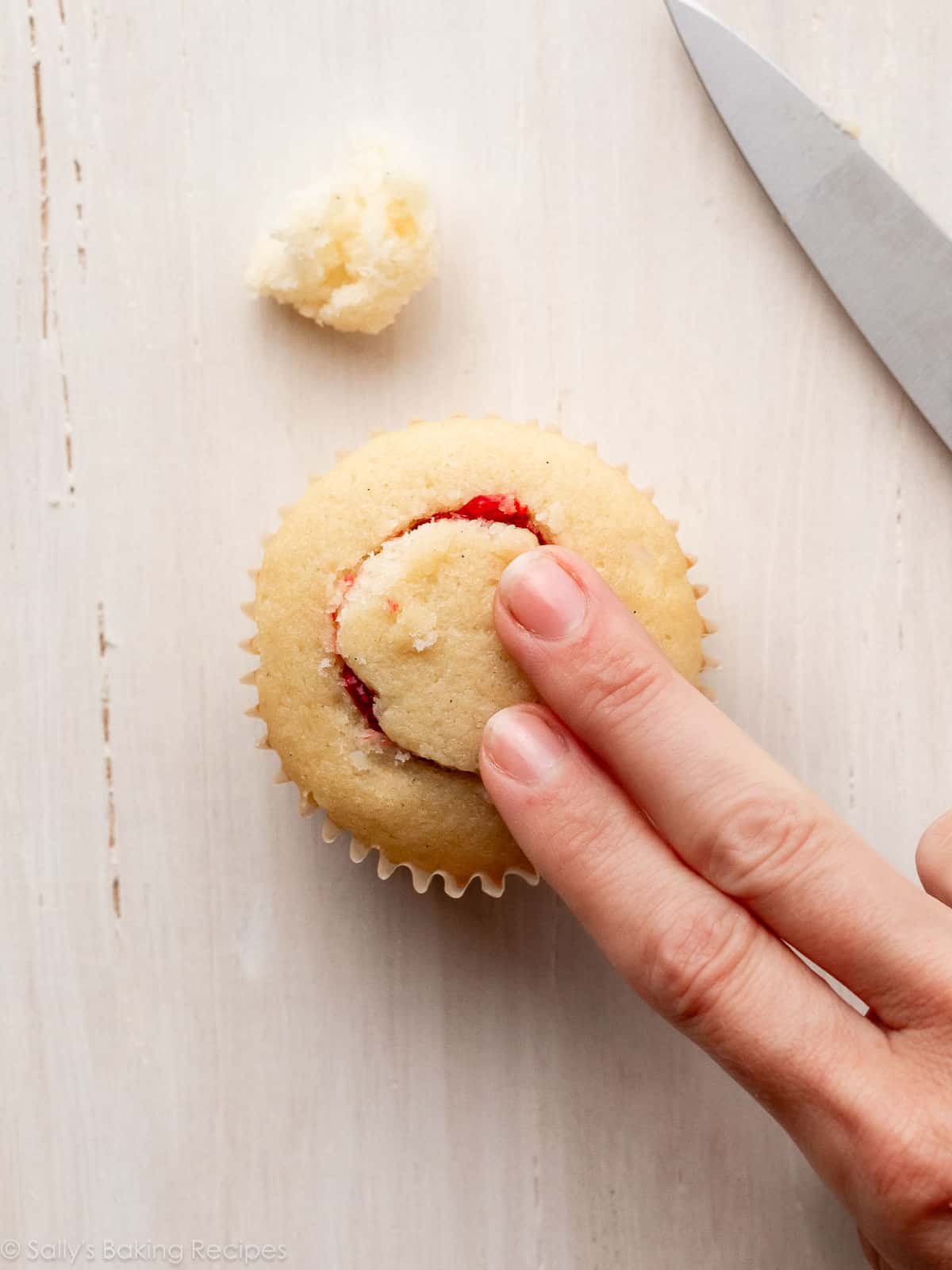 two fingers on cupcake that has filling inside.