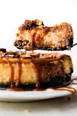 slice of Snickers cheesecake being removed from full cheesecake on a dessert serving utensil