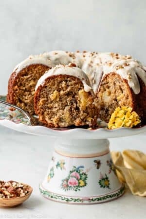 slice of hummingbird Bundt cake with icing and yellow flowers on cake stand.