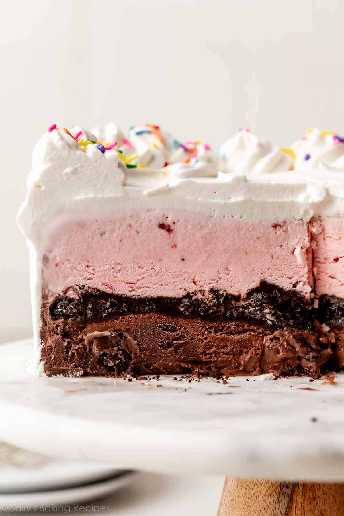 strawberry, Oreo crunch, and chocolate ice cream cake sliced on cake stand.