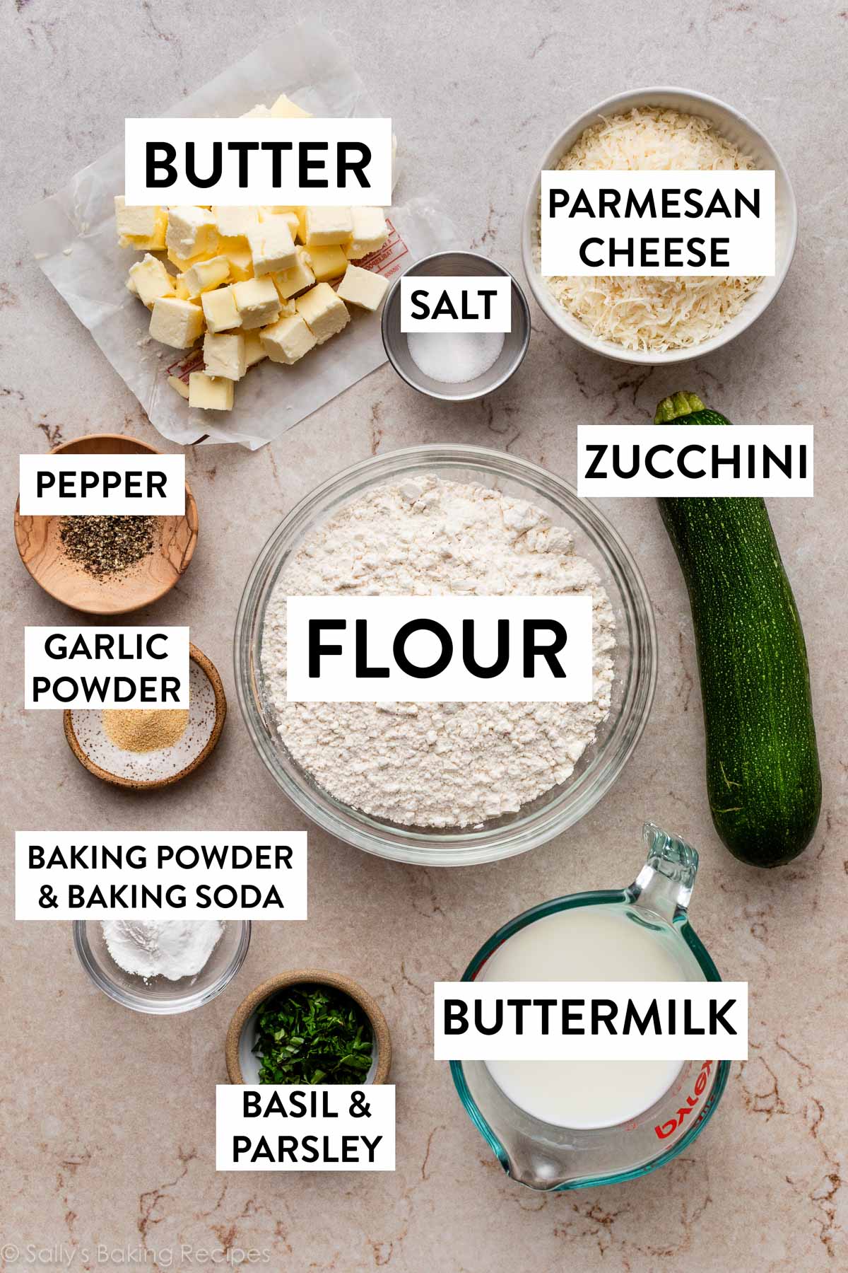 ingredients measured out on counter including big bowl of flour, shredded parmesan cheese, cubed butter, liquid measuring cup of buttermilk, and fresh herbs.