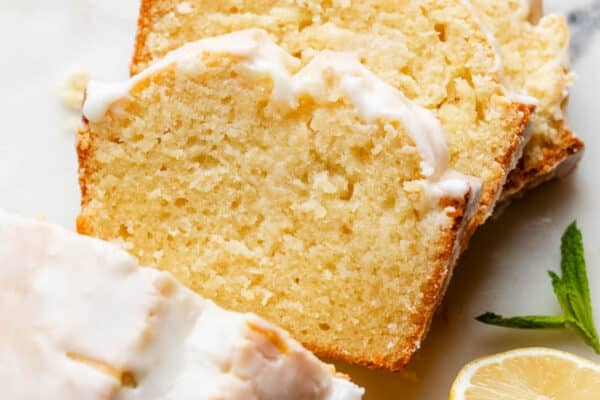 iced lemon pound cake loaf slices on marble board with lemons on the side.