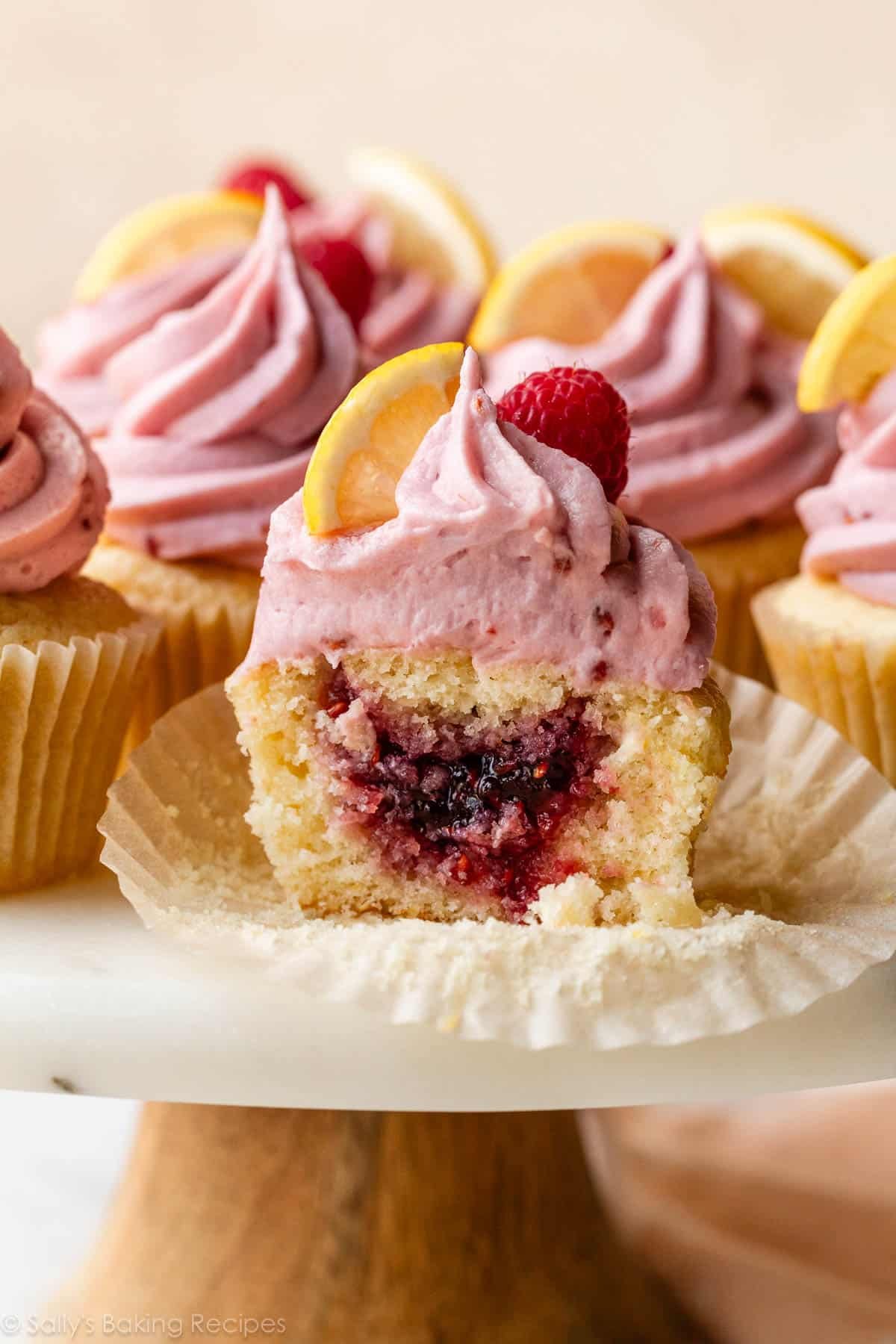 lemon raspberry jam-filled cupcakes with raspberry frosting on cupcake wrapper on cake stand.