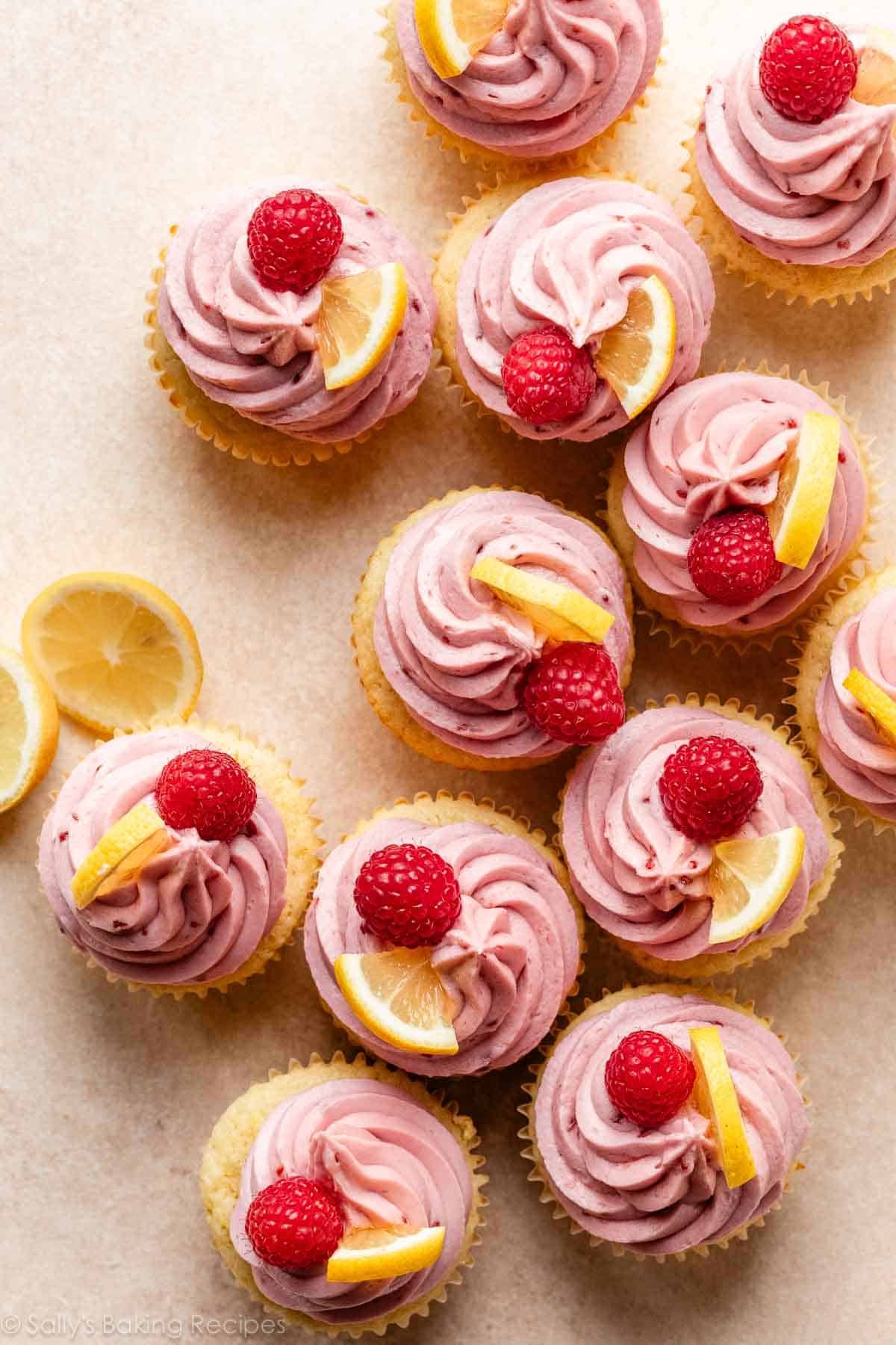 overhead photo of lemon raspberry cupcakes with lemon slices and fresh raspberries on top.